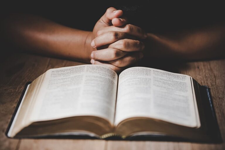 Person praying with hands folded over an open Bible