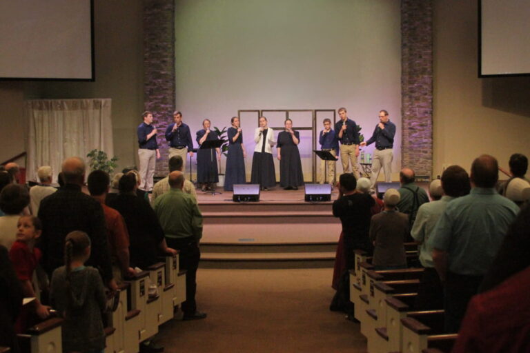 Congregation standing during a church service while a singing group leads worship on stage.
