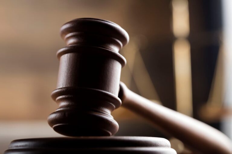 Close-up of a dark wooden judge's gavel resting on its round sound block against a warm, softly blurred courtroom background.